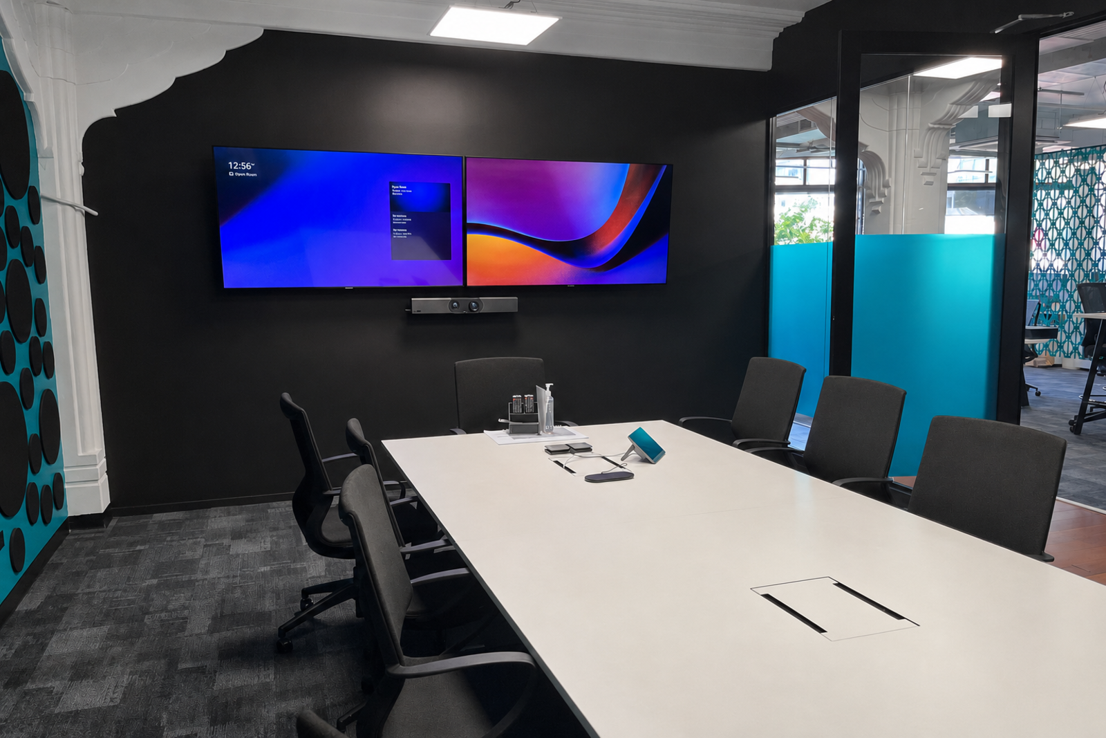 A boardroom with dual wall-mounted displays, a video bar and a conference speakerphone on the table