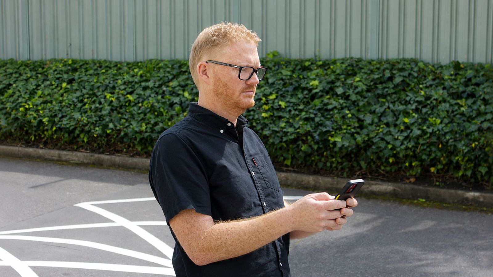 A man standing outside an office checking a sign-in approval on his phone